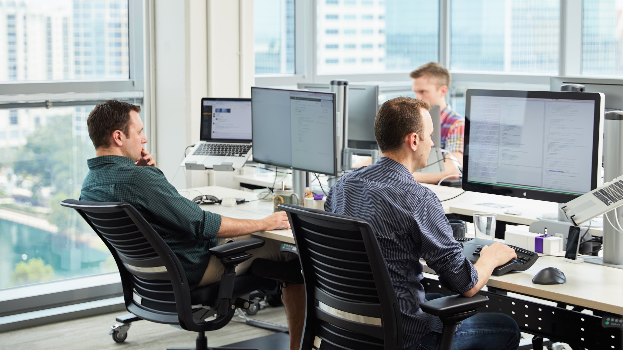 Three Envy Labs developers coding from their respective workstations in a bright office